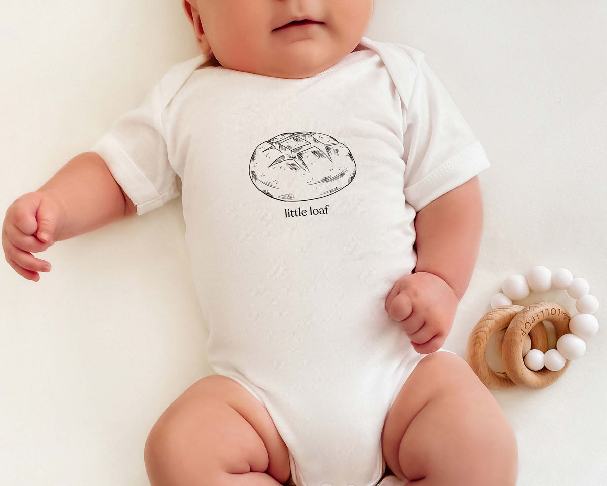 Baby wearing a onesie with a sourdough bread graphic and the text 'little loaf'.