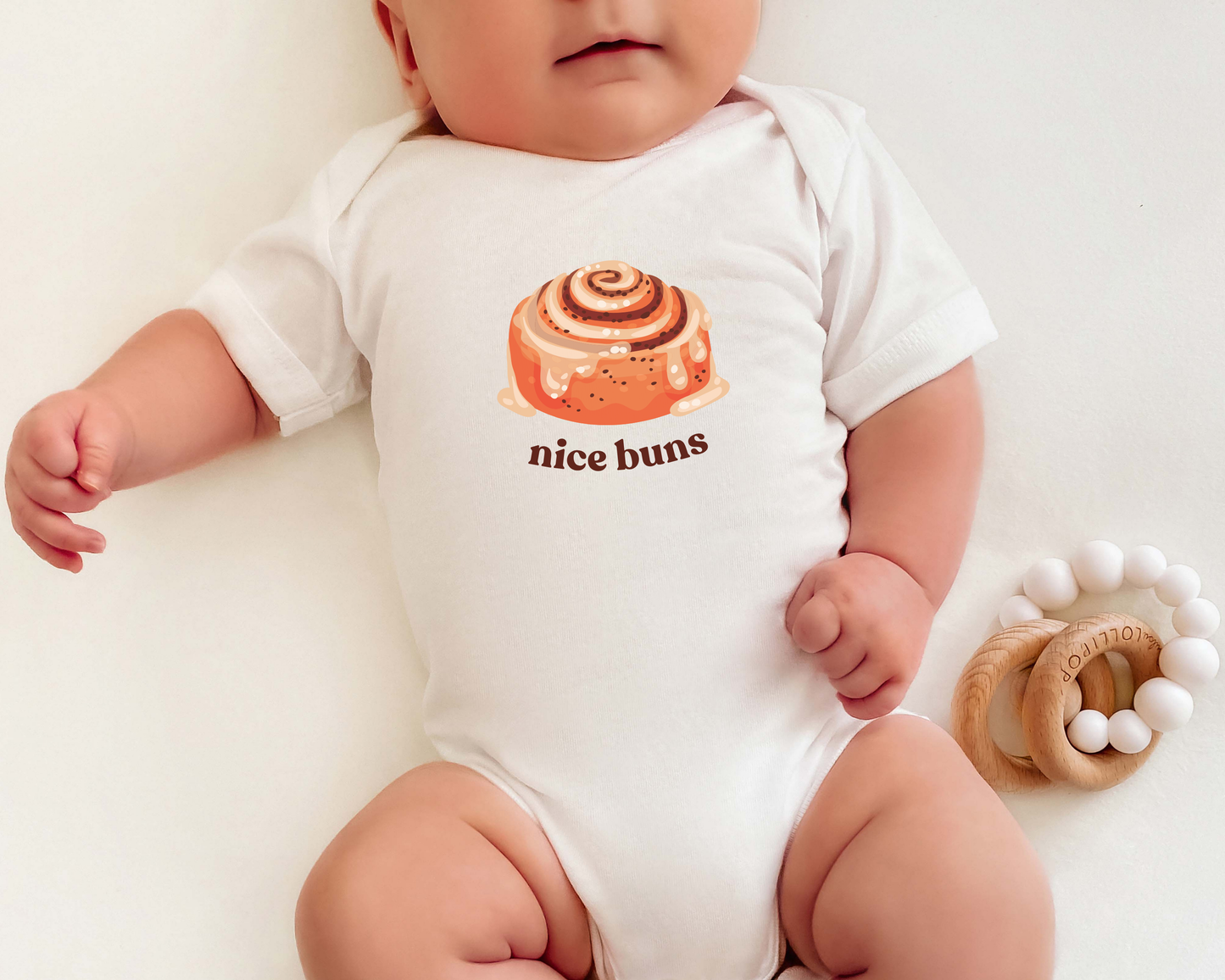 A baby wearing a short sleeve cotton baby onesie with a cinnamon bun graphic and the text "nice buns".