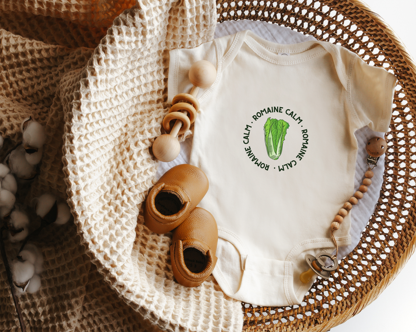 A cotton baby onesie with a graphic of fresh green romaine lettuce and the text "romaine calm".