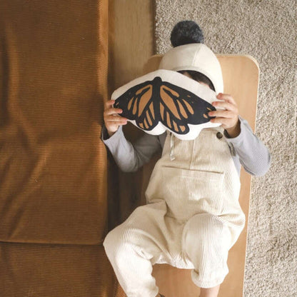 Child holding a butterfly-shaped pillow in front of their face.