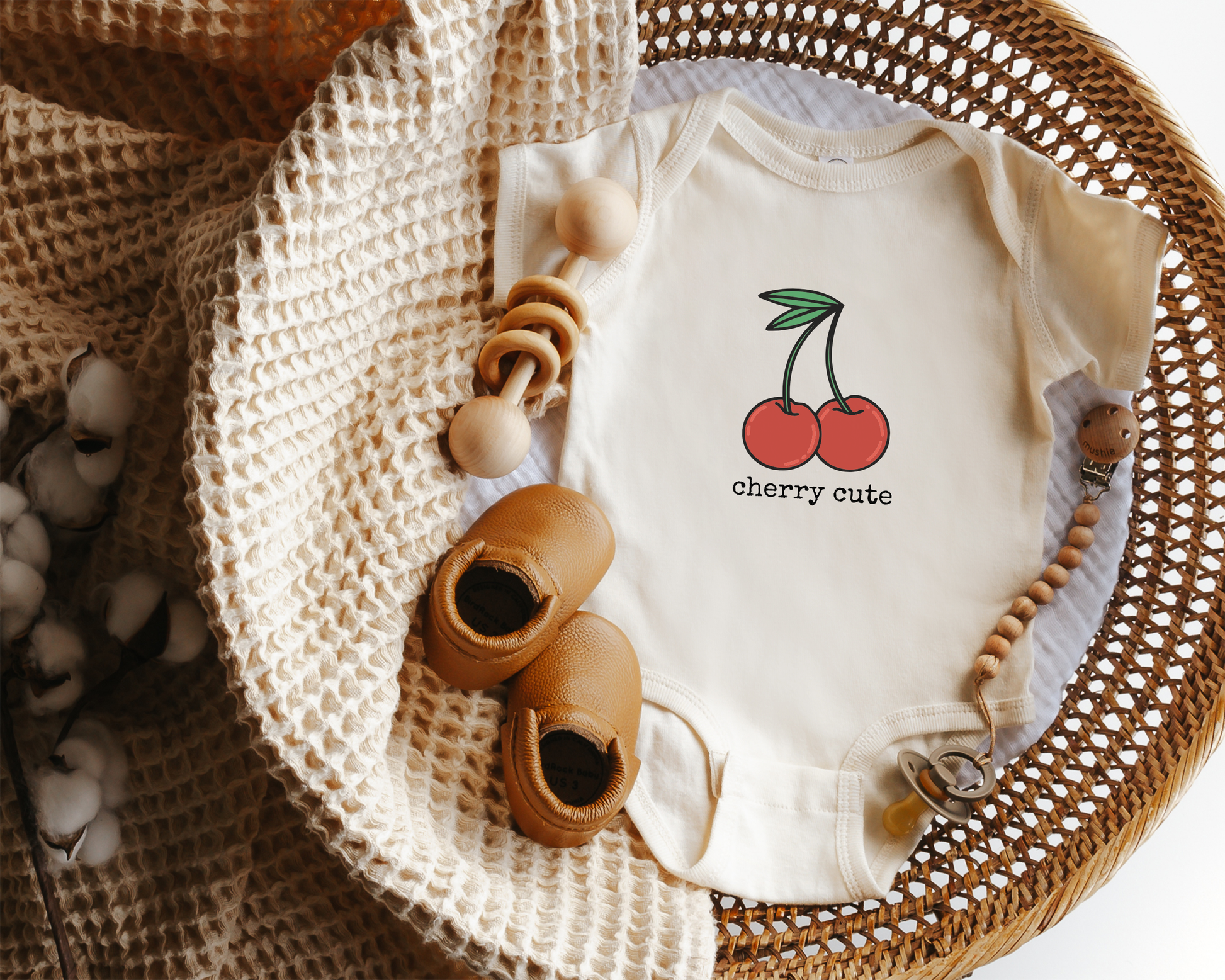 Baby onesie with cherry graphic and the text "cherry cute" styled in a basket.