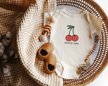 Baby onesie with cherry graphic and the text "cherry cute" styled in a basket.