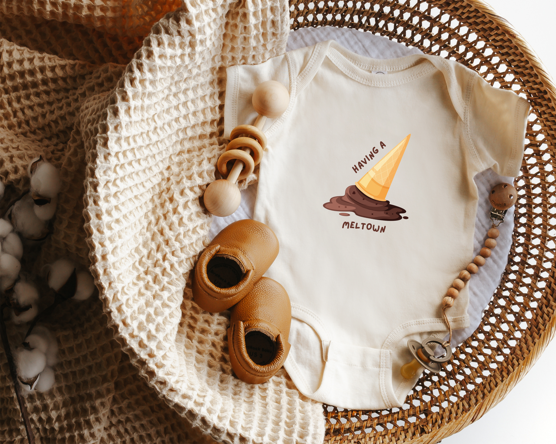 A short sleeve cotton baby onesie with a graphic of a melting ice cream cone and the text "having a meltdown" styled in a basket.