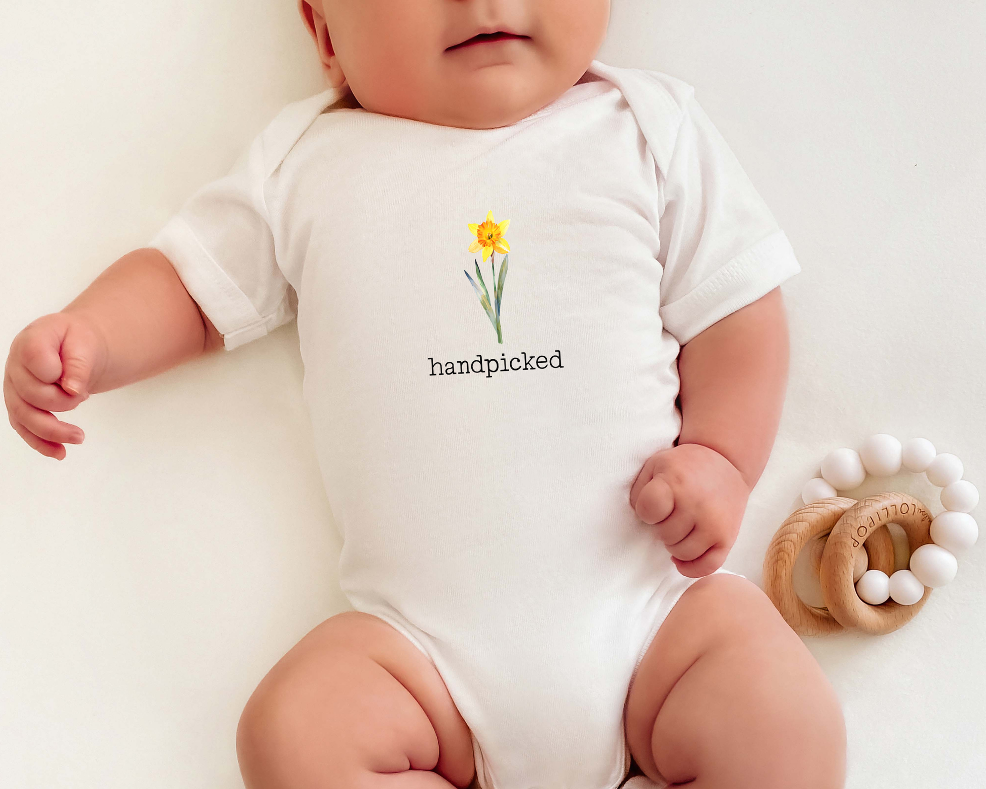 Short sleeve cotton onesie with a graphic of a the March birth flower, a daffodil, and the text "handpicked"