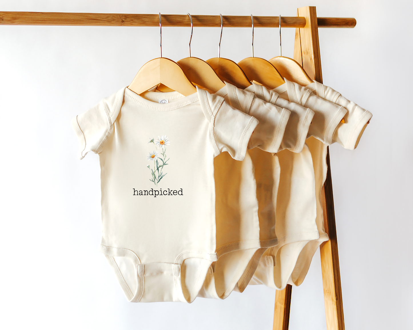 Short sleeve cotton baby onesie with daisy, the April birth flower, graphic and the text "handpicked".