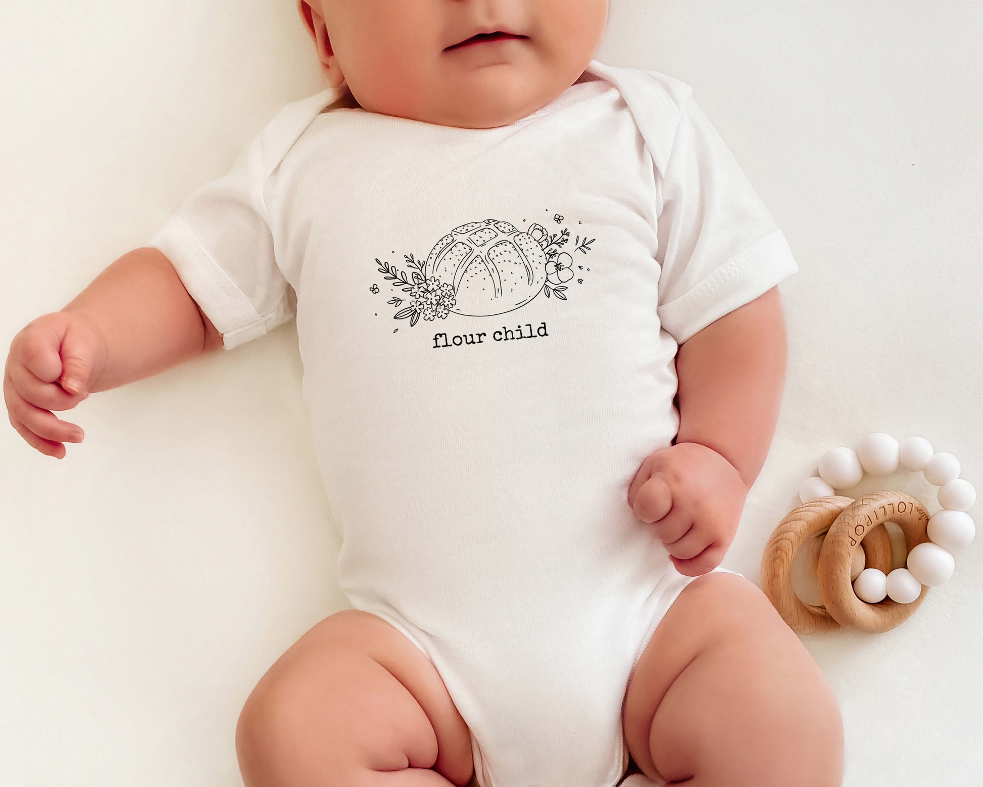 Baby wearing a white onesie with 'flour child' print on a light background