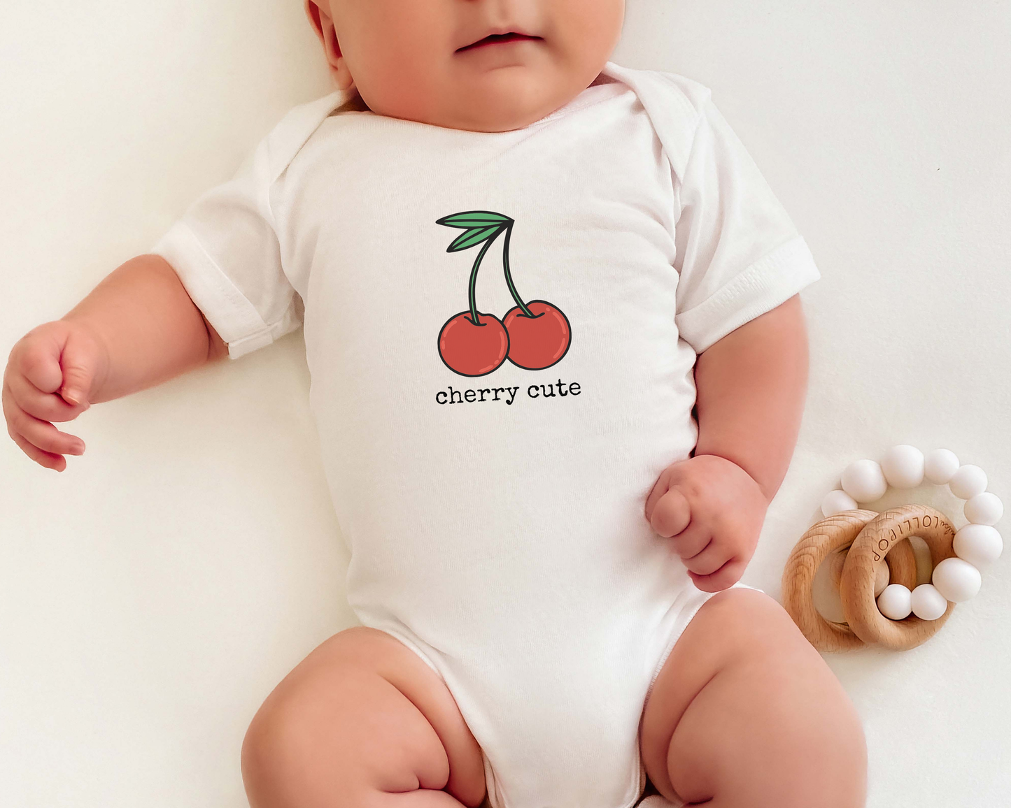 Baby wearing a white onesie with a cherry graphic and the text "cherry cute" on it.