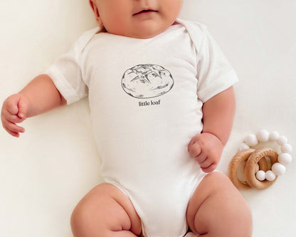 Baby wearing a onesie with a sourdough bread graphic and the text 'little loaf'.
