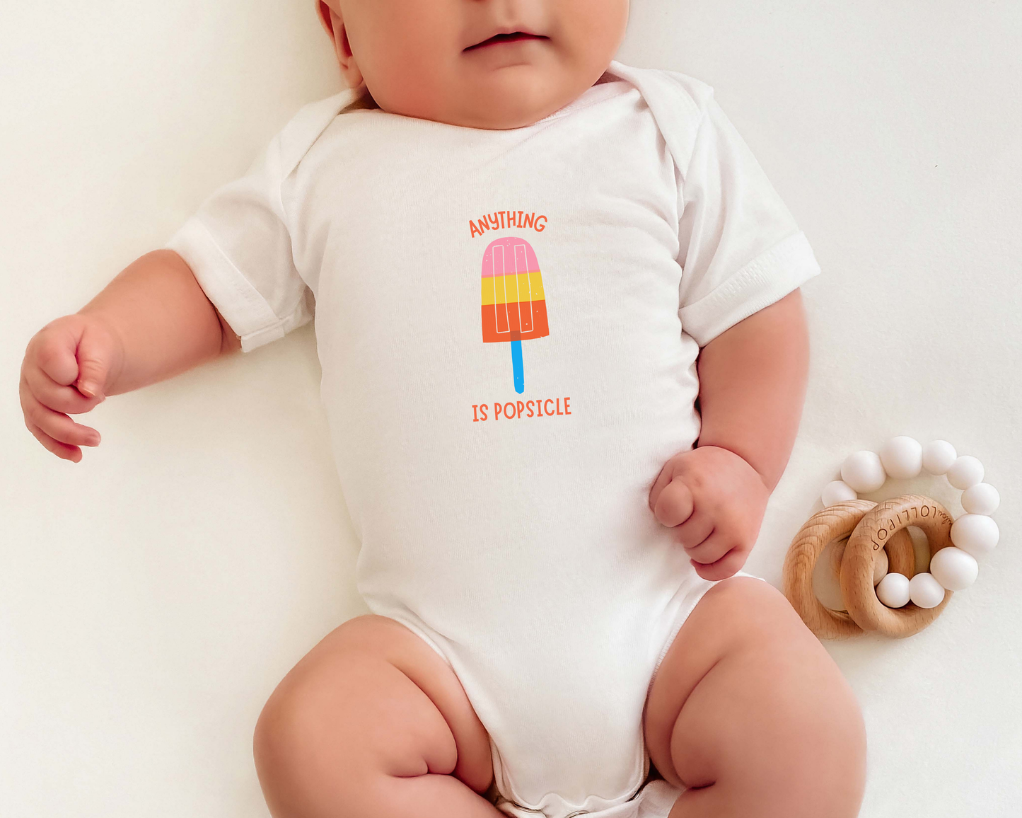 A baby wearing a short sleeve cotton baby onesie with a colorful popsicle graphic and the text "anything is popsicle".