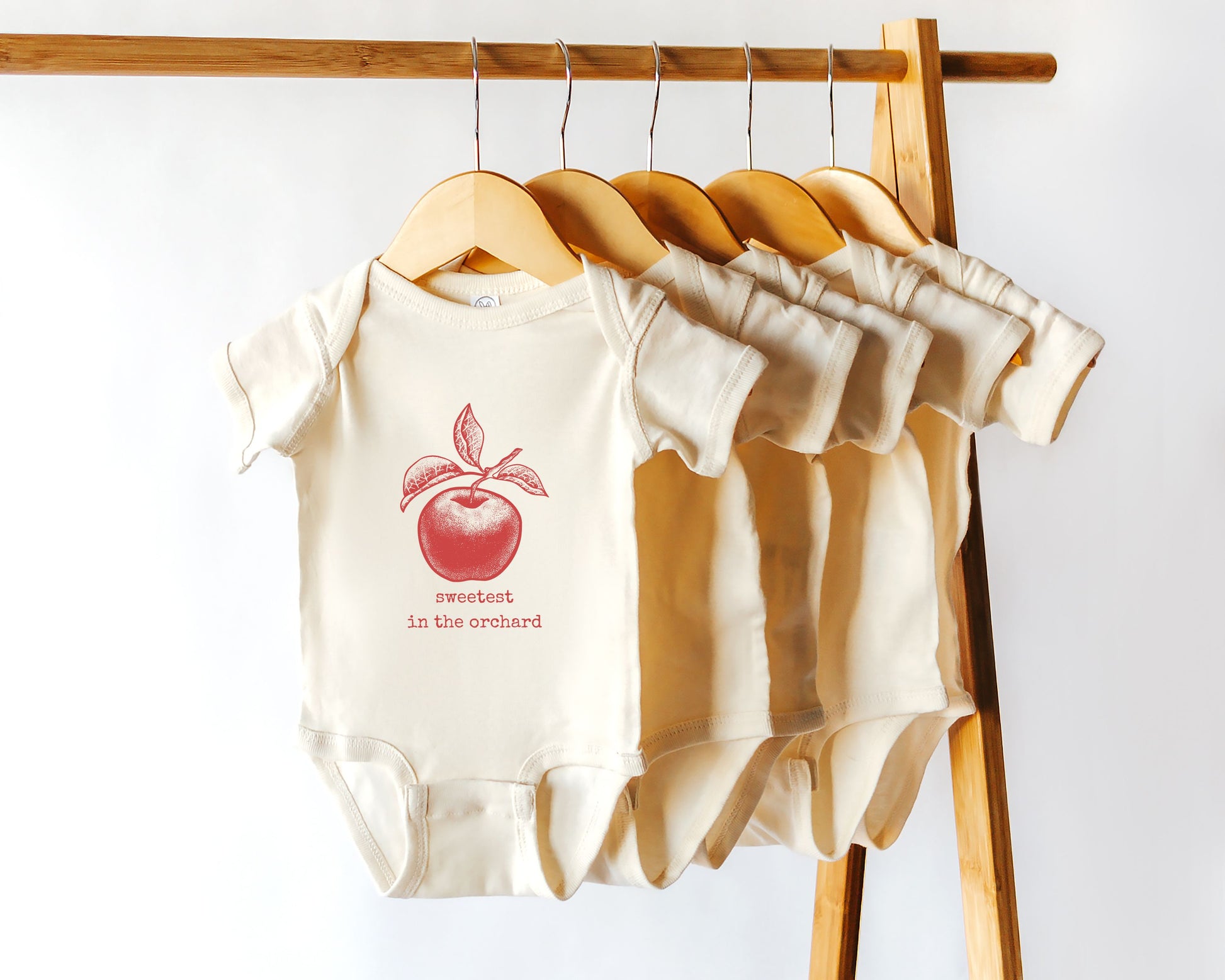 Short sleeve cotton onesie with a distressed style graphic of an apple in red with the text sweetest in the orchard in a typewriter style font.