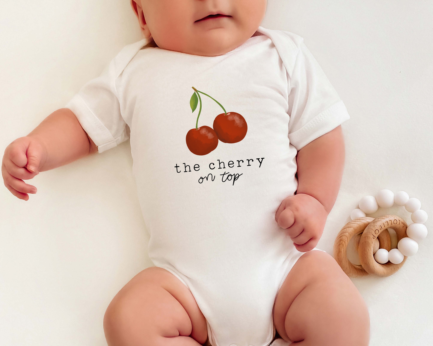 Baby wearing a cotton onesie with cherry graphic and the text "the cherry on top".