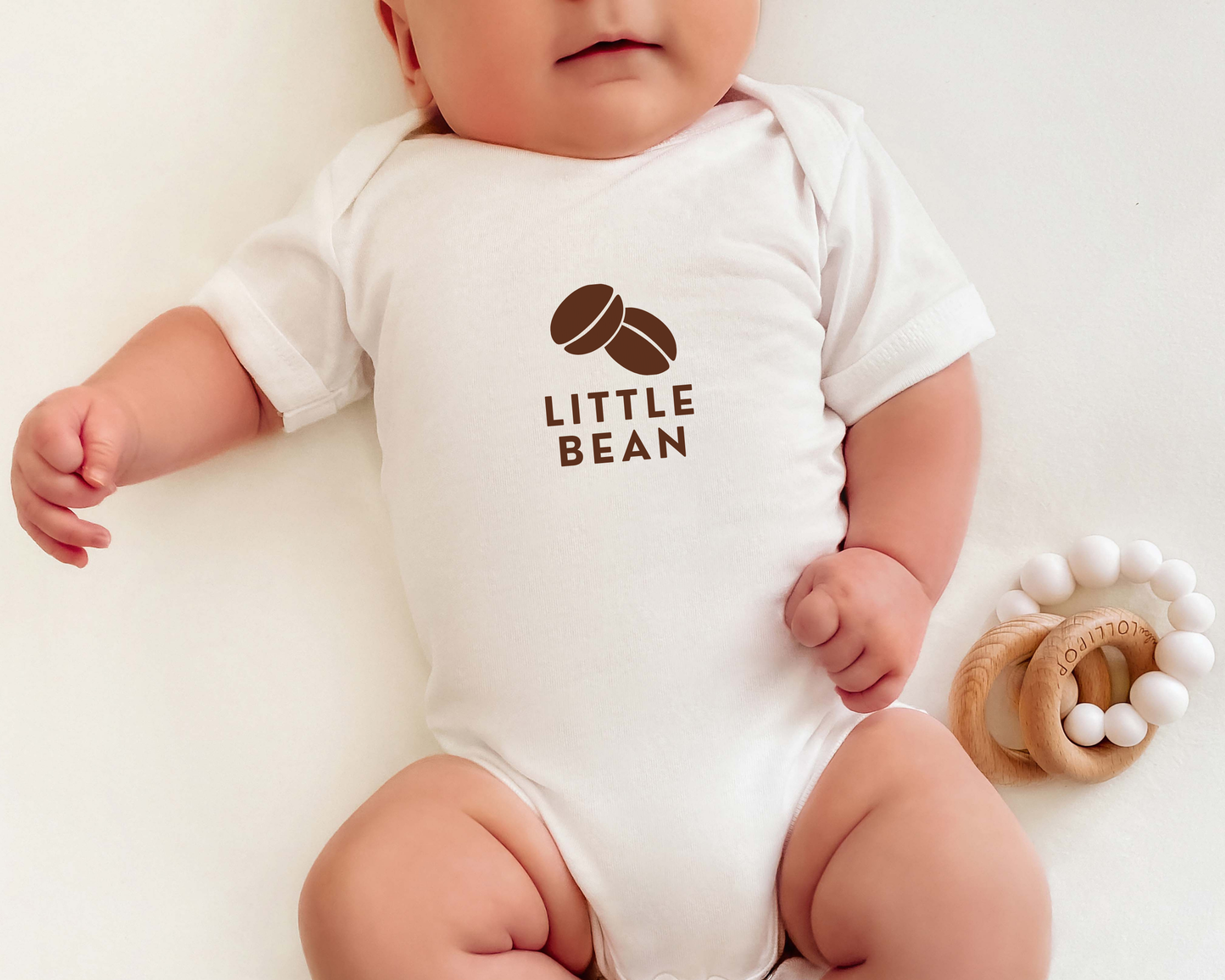 A baby wearing a short sleeve coffee themed baby onesie with a coffee bean graphic and the text little bean.