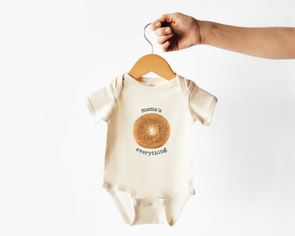 Short sleeve cotton baby onesie with an everything bagel graphic and the text "mama's everything" on a hanger.