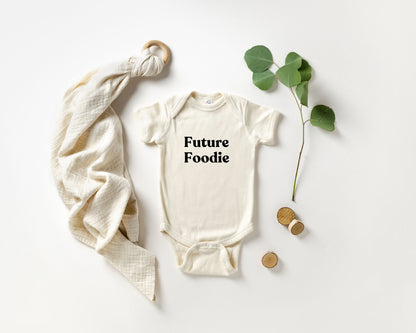 Baby onesie with 'Future Foodie' text on a white background with a blanket and leaves.