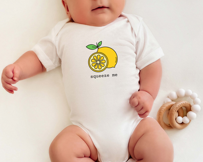 Baby wearing a short sleeve, white, cotton onesie with a lemon graphic and the text "squeeze me"on it.