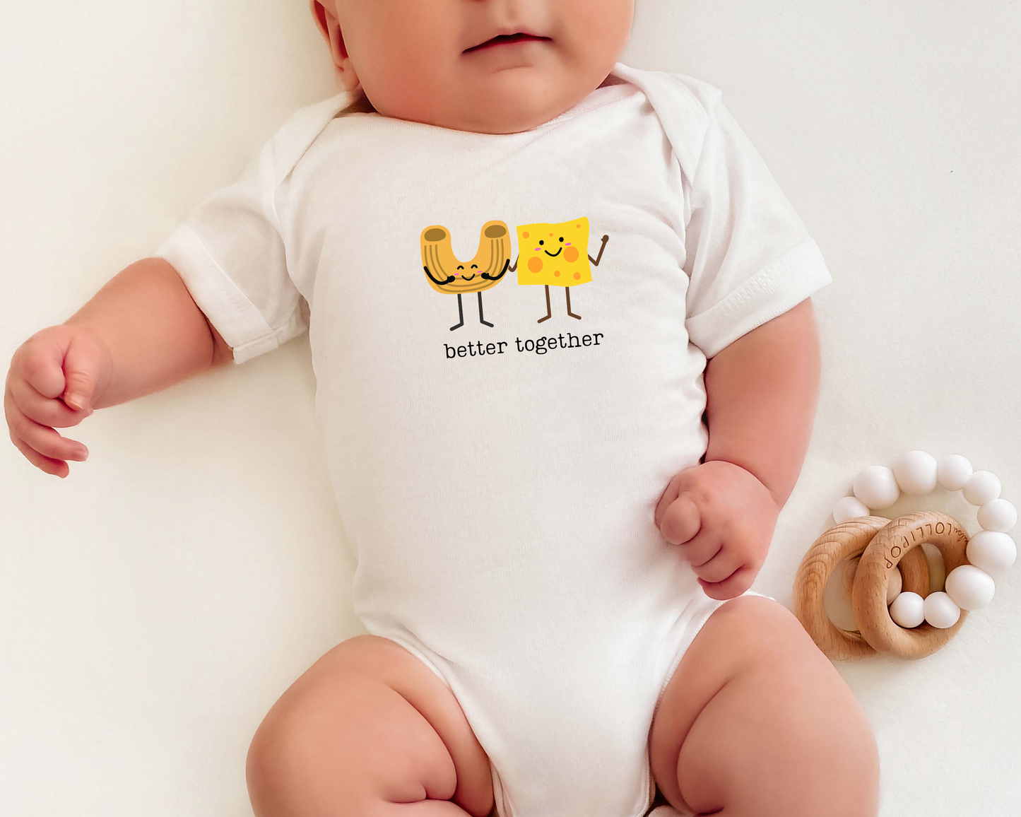 Photo of a baby wearing a short sleeve cotton baby onesie with a cute graphic of a macaroni noodle and cheese with the phrase "better together".