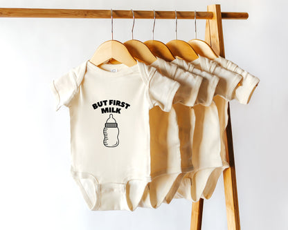 Short sleeve cotton baby onesie with a baby bottle graphic and the text but first milk