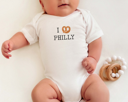 Baby wearing an short sleeve cotton bodysuit with a soft pretzel graphic for an I Heart Philly message.