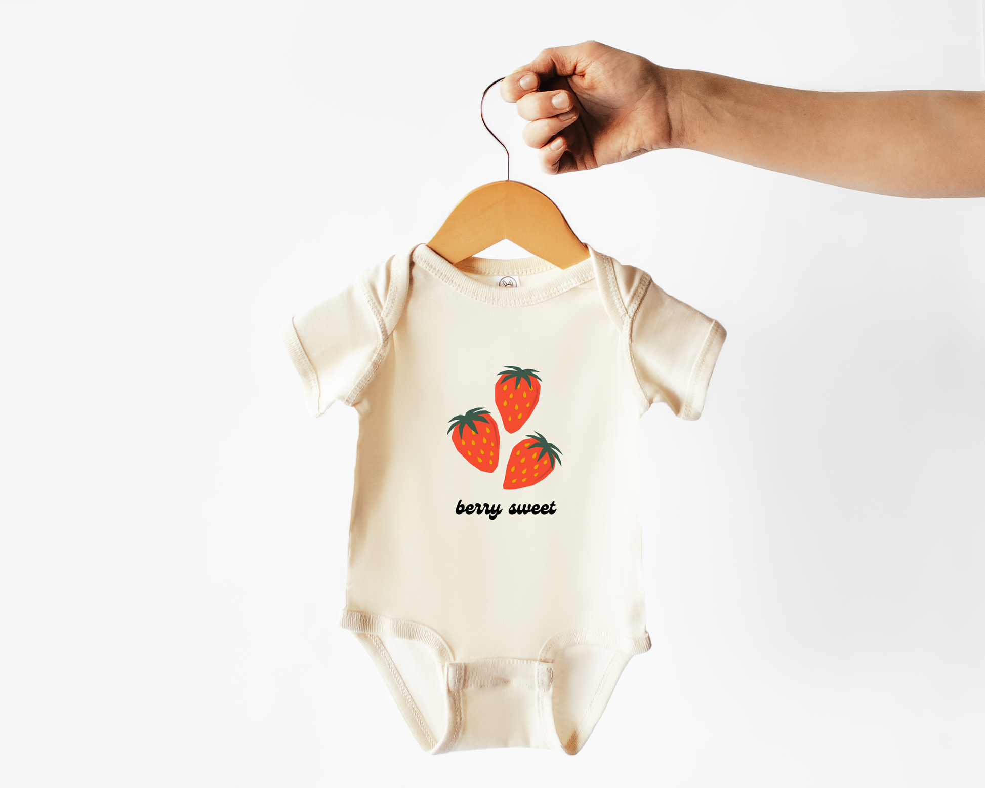 A short sleeve cotton baby bodysuit with strawberry fruit graphics and the text "berry sweet" shown on a wooden hanger. 