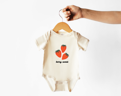 A short sleeve cotton baby bodysuit with strawberry fruit graphics and the text "berry sweet" shown on a wooden hanger. 