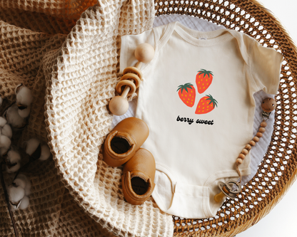 A short sleeve cotton baby onesie with red strawberry graphics and the text "berry sweet" displayed in a wicker basket.