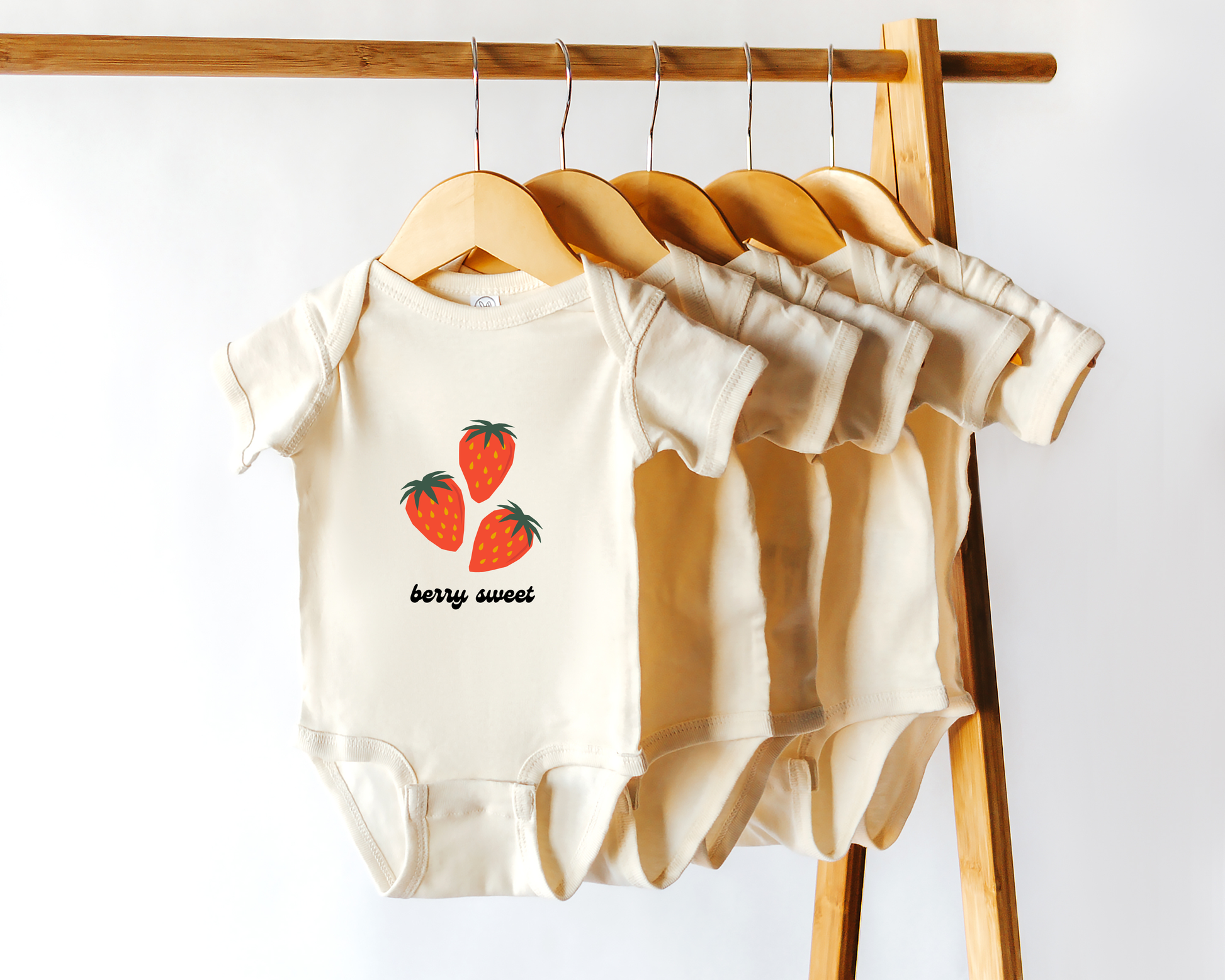 A short sleeve cotton baby onesie with strawberry fruit graphics and the text "berry sweet". Displayed in wooden hanger.