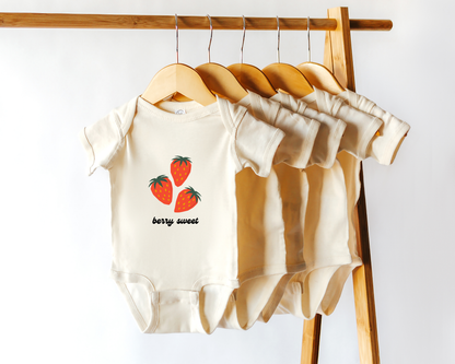 A short sleeve cotton baby onesie with strawberry fruit graphics and the text "berry sweet". Displayed in wooden hanger.