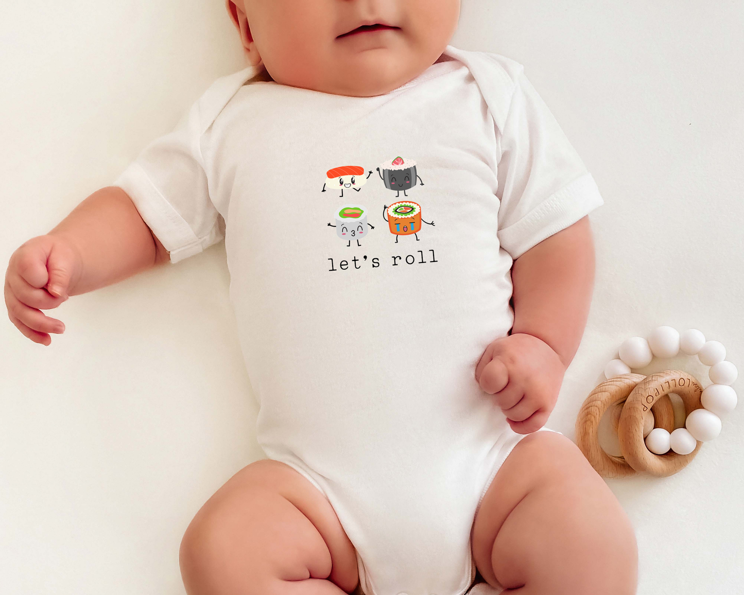 Baby wearing a short sleeve cotton onesie with sushi graphics on it and the text "let's roll".